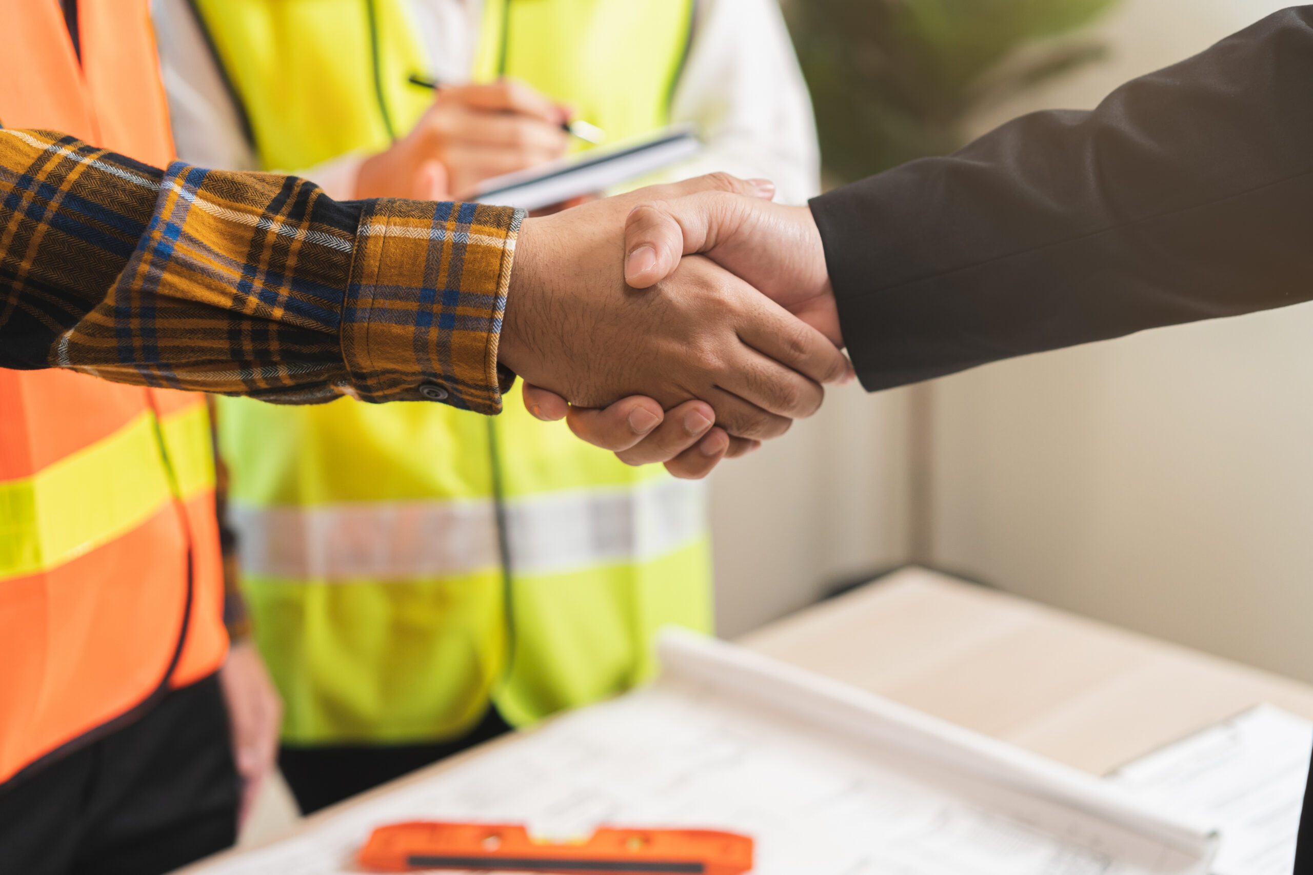Handshake between construction worker and businessman over blueprints