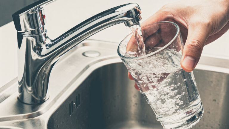 Vaso llenándose con agua del grifo en el fregadero de la cocina