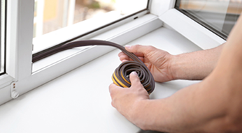 Hands applying weatherstripping to window frame