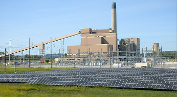 Solar panel farm with power plant in background